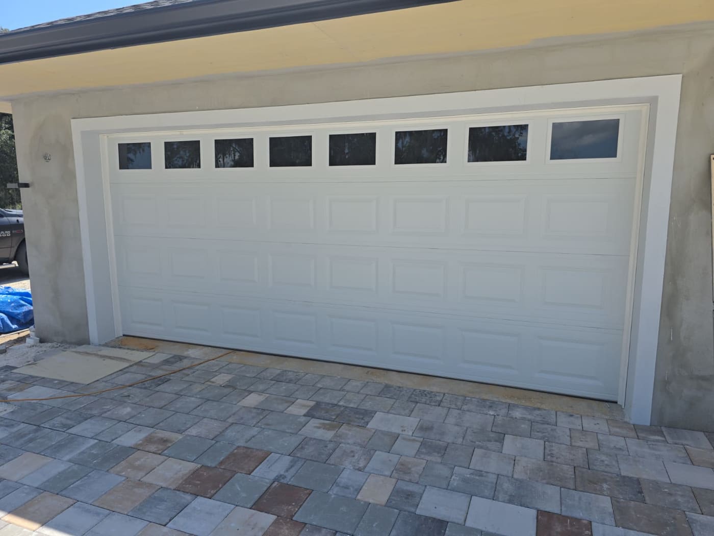 A white raised-panel double garage door with a row of eight small windows across the top, seen from the driveway of a finished house.