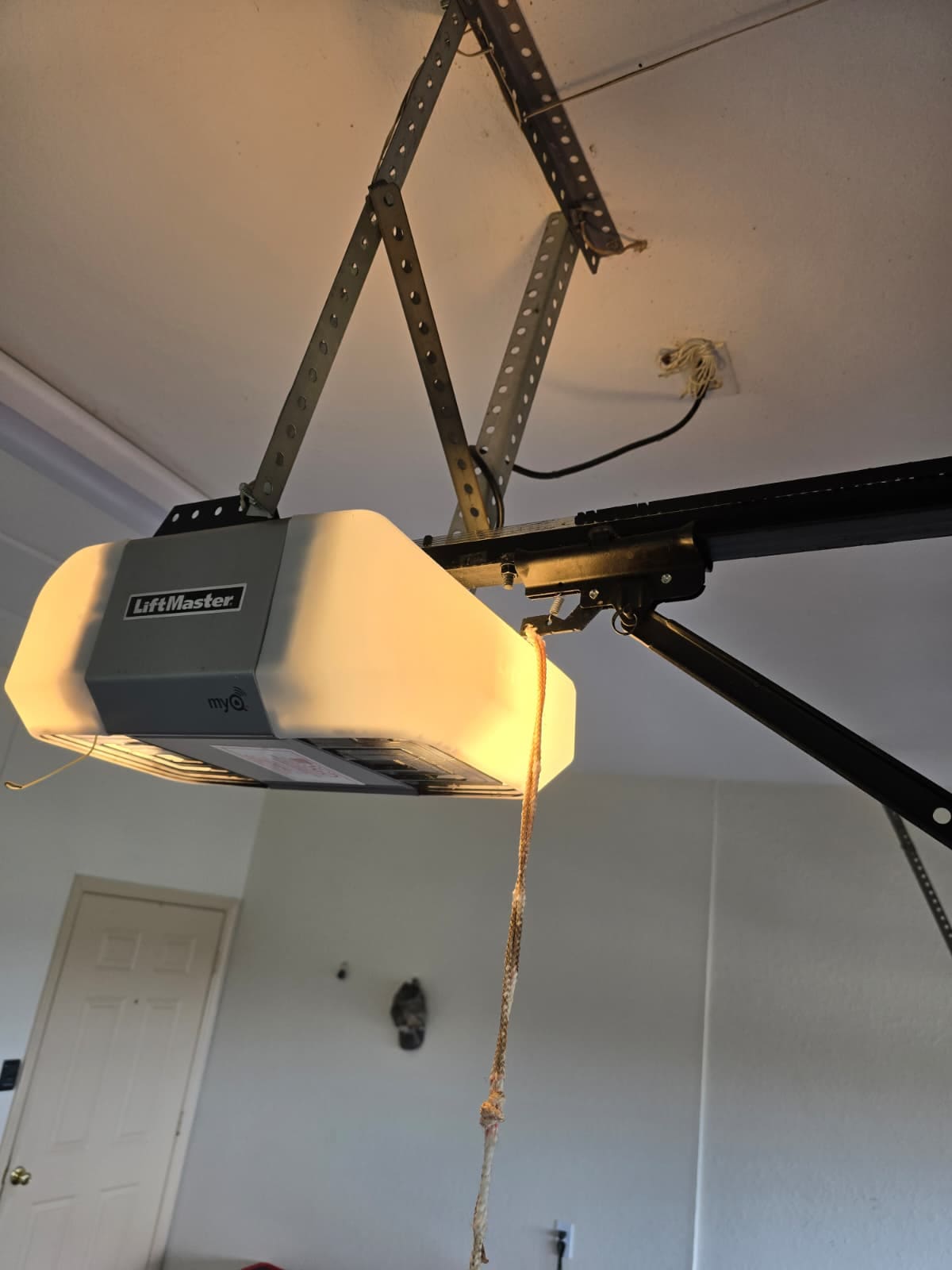 A garage door opener mounted to a ceiling, photographed from below, with its rail and drive running away towards the door.