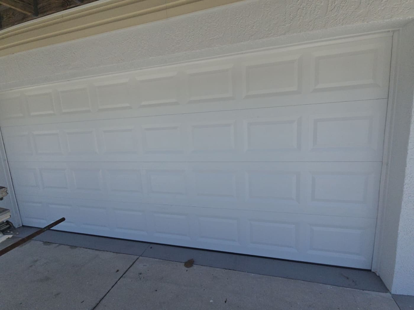 A white raised-panel double garage door in a cream stucco wall, photographed square-on from the driveway.