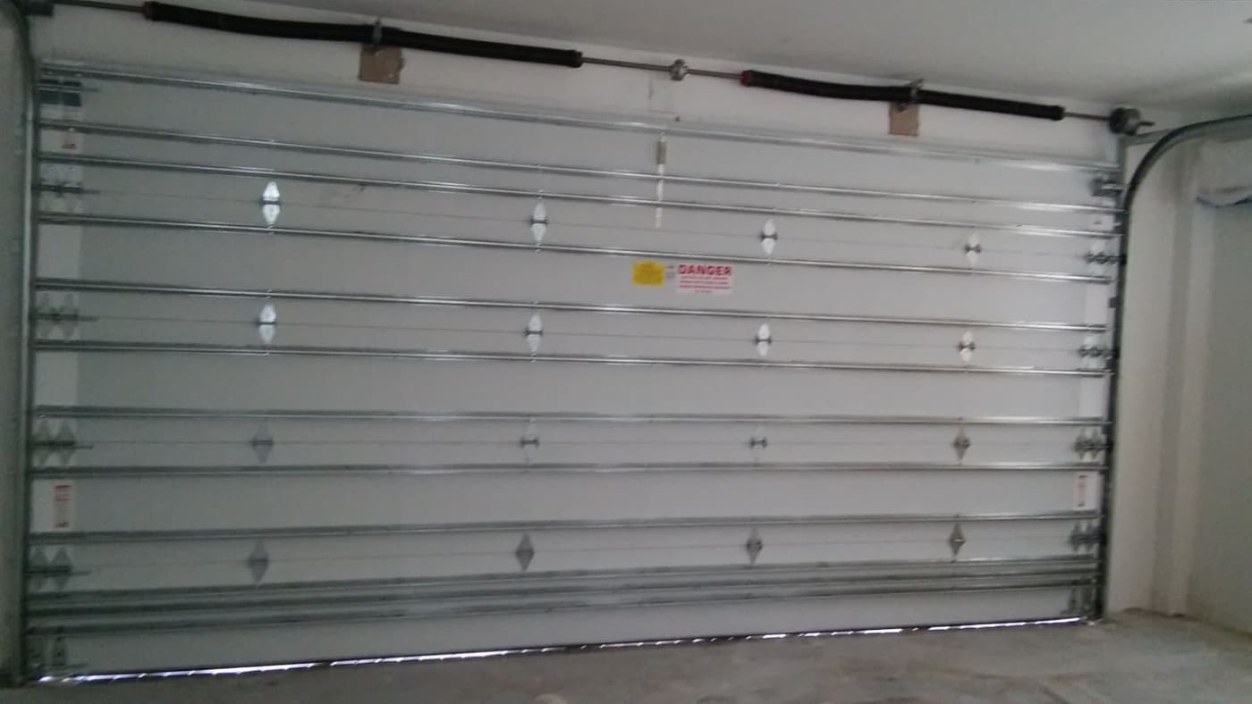 The inside face of a garage door with steel bracing across the panels and red and yellow warning labels on it.
