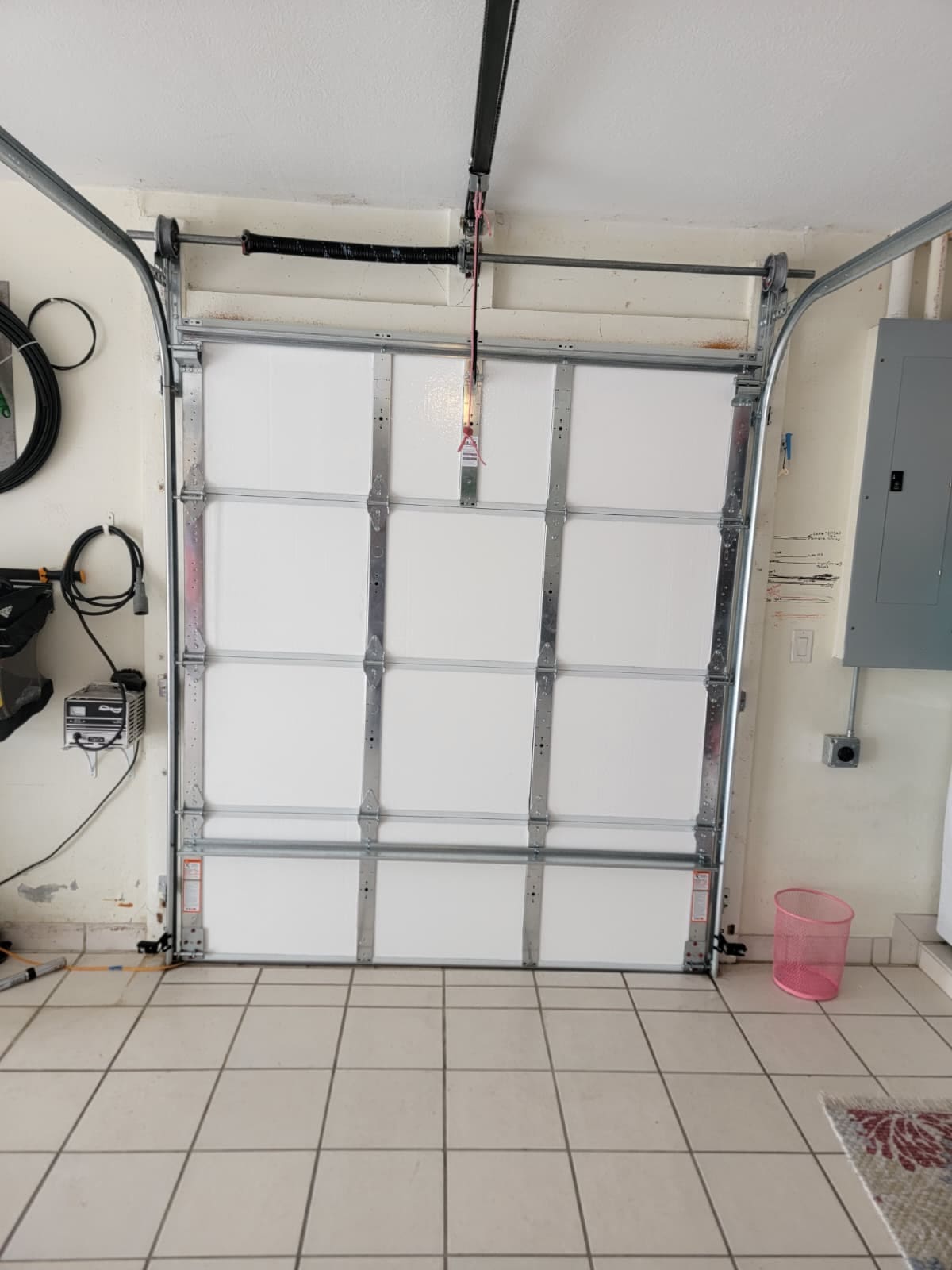 A white garage door seen from inside with steel struts across it, an electrical panel on the wall beside the opening and the track running up to the ceiling.