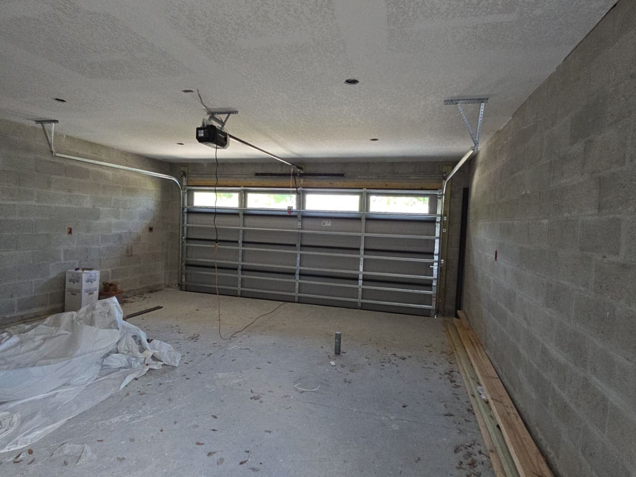 A garage door with a row of windows across the top, seen from inside a block-walled garage under construction, with the opener mounted to the ceiling.